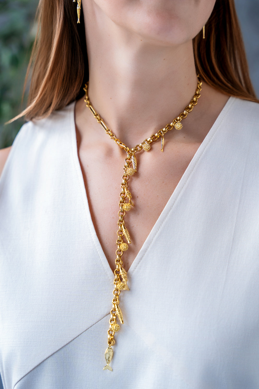 Convertible gold fish charm necklace with dangling fish and textured bead charms worn as both a lariat and classic chain necklace.