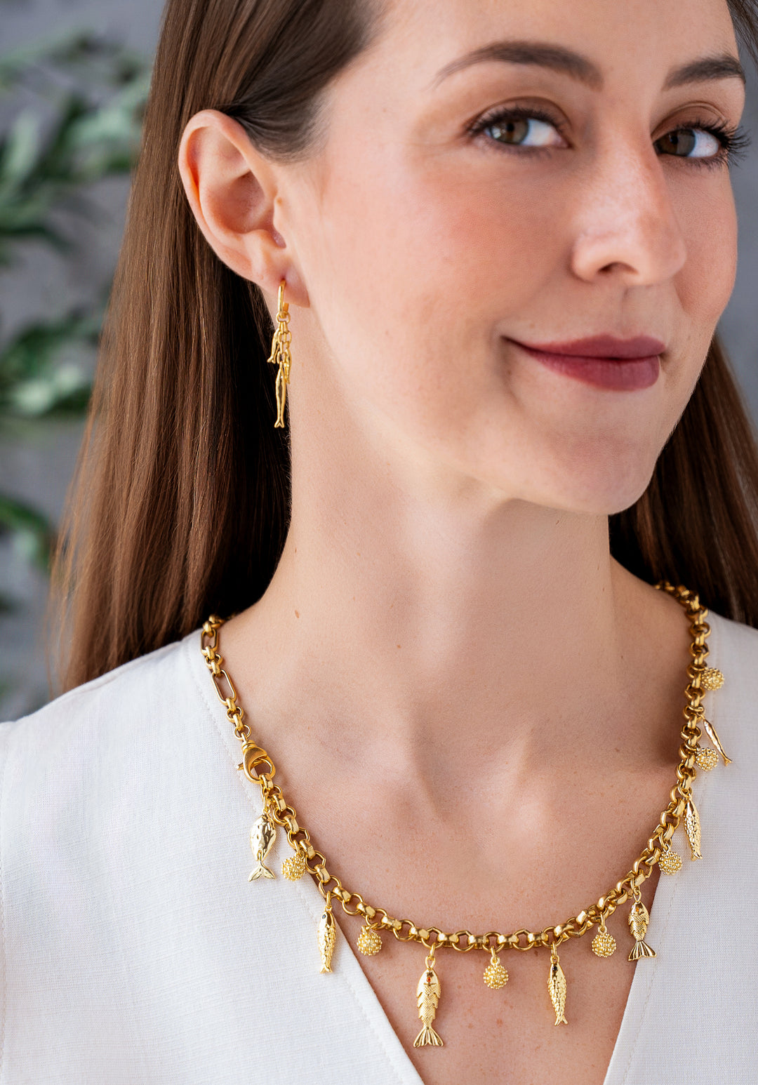 Convertible gold fish charm necklace with dangling fish and textured bead charms worn as both a lariat and classic chain necklace.