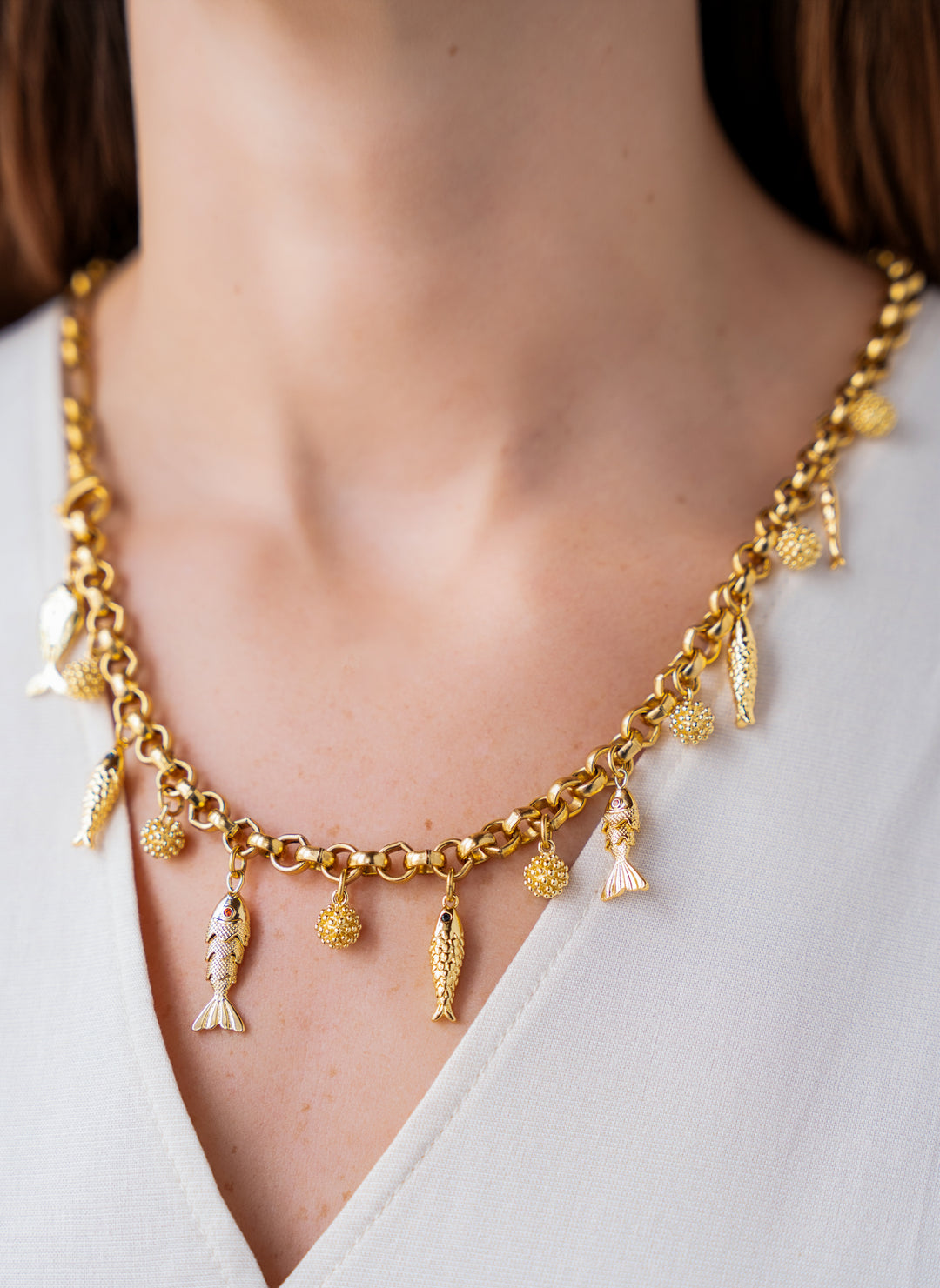 Convertible gold fish charm necklace with dangling fish and textured bead charms worn as both a lariat and classic chain necklace.