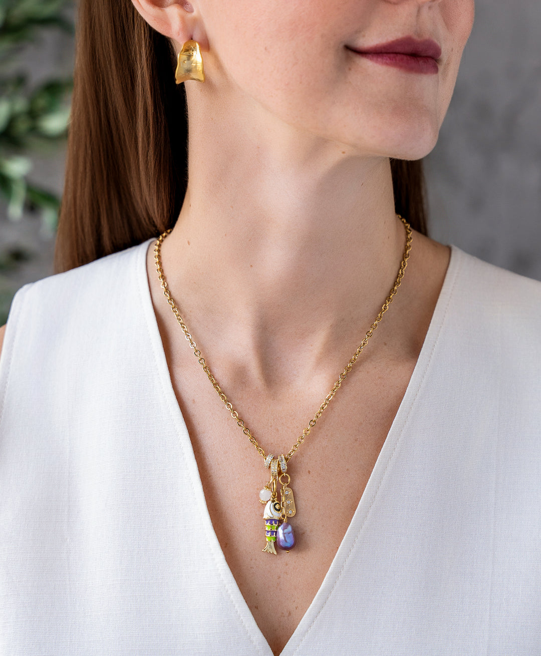 Gold charm necklace with enamel fish charm, freshwater pearl drop, and pavé accent charms on a delicate chain.