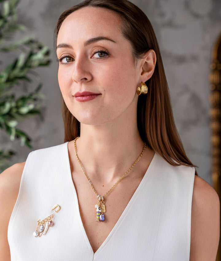 Gold charm necklace with enamel fish charm, freshwater pearl drop, and pavé accent charms on a delicate chain.