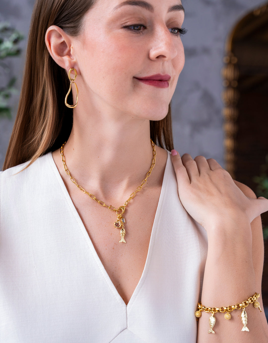 Gold chain necklace with fish charm, pomegranate charm, and crystal accents.