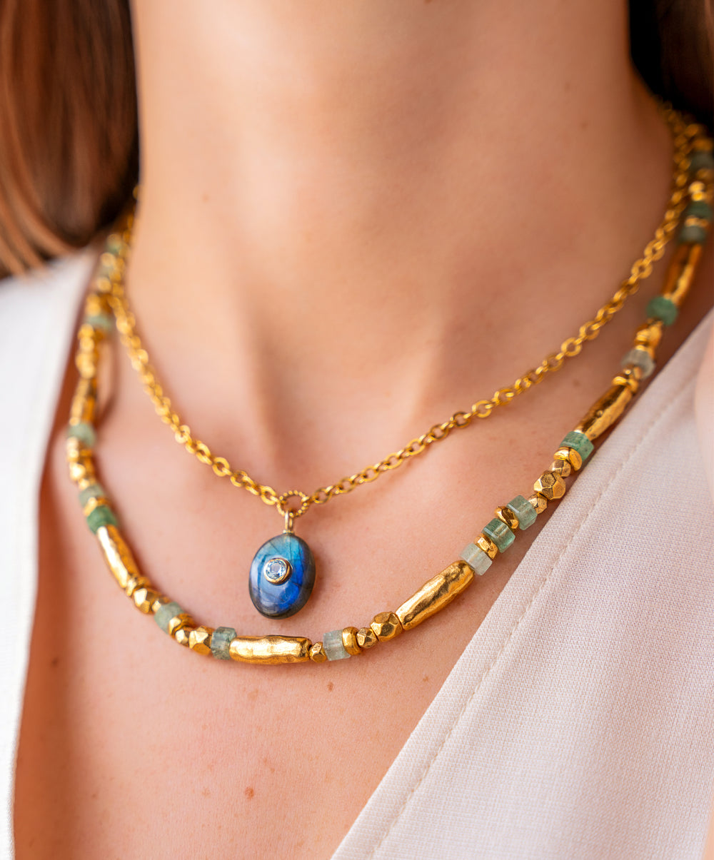 Oval labradorite pendant necklace with blue topaz inlay on a gold chain.