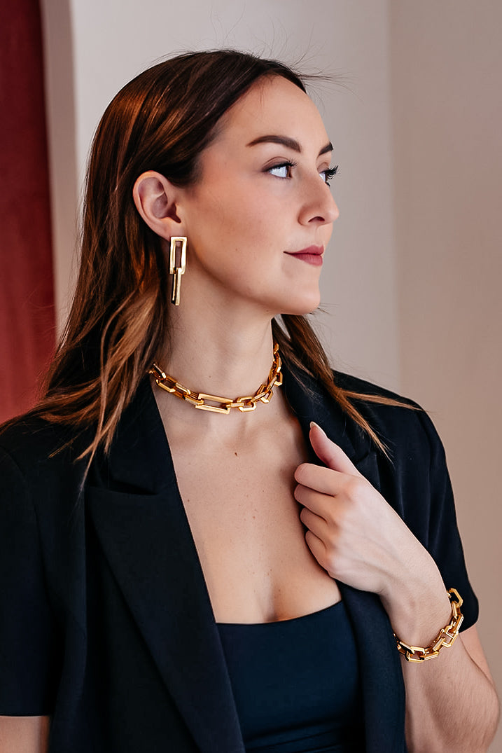 A model wearing A gold dangle earring with interlocking rectangle shapes.