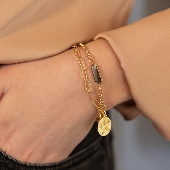 A model wearing A two strand matte gold bracelet with baguette shaped labradorite gemstones and a sun and moon charm