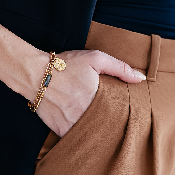 A model wearing A two strand matte gold bracelet with baguette shaped labradorite gemstones and a sun and moon charm