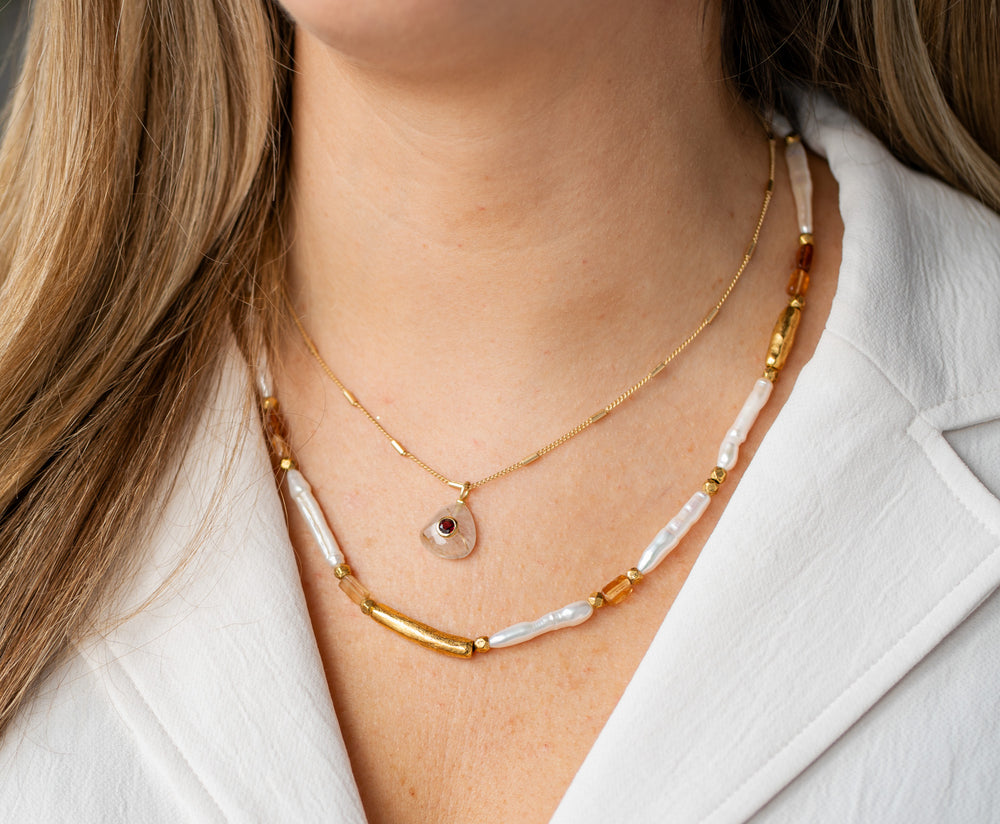 Gold chain necklace with a teardrop-shaped rutilated quartz pendant featuring a deep red garnet inlay