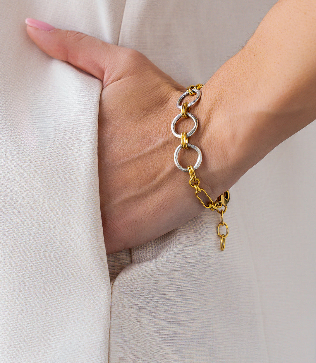 Mixed metal bracelet with oversized gold and silver rings connected by twisted rope links and chain details.