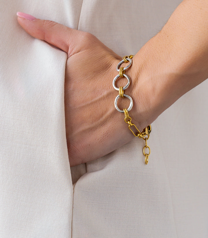 Mixed metal bracelet with oversized gold and silver rings connected by twisted rope links and chain details.