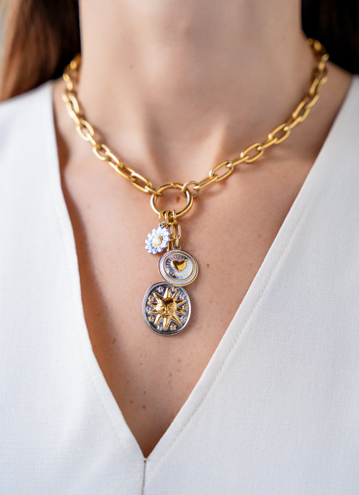 Mixed metal charm cluster necklace with sun medallion, heart charm, and daisy charm on a gold paperclip chain.