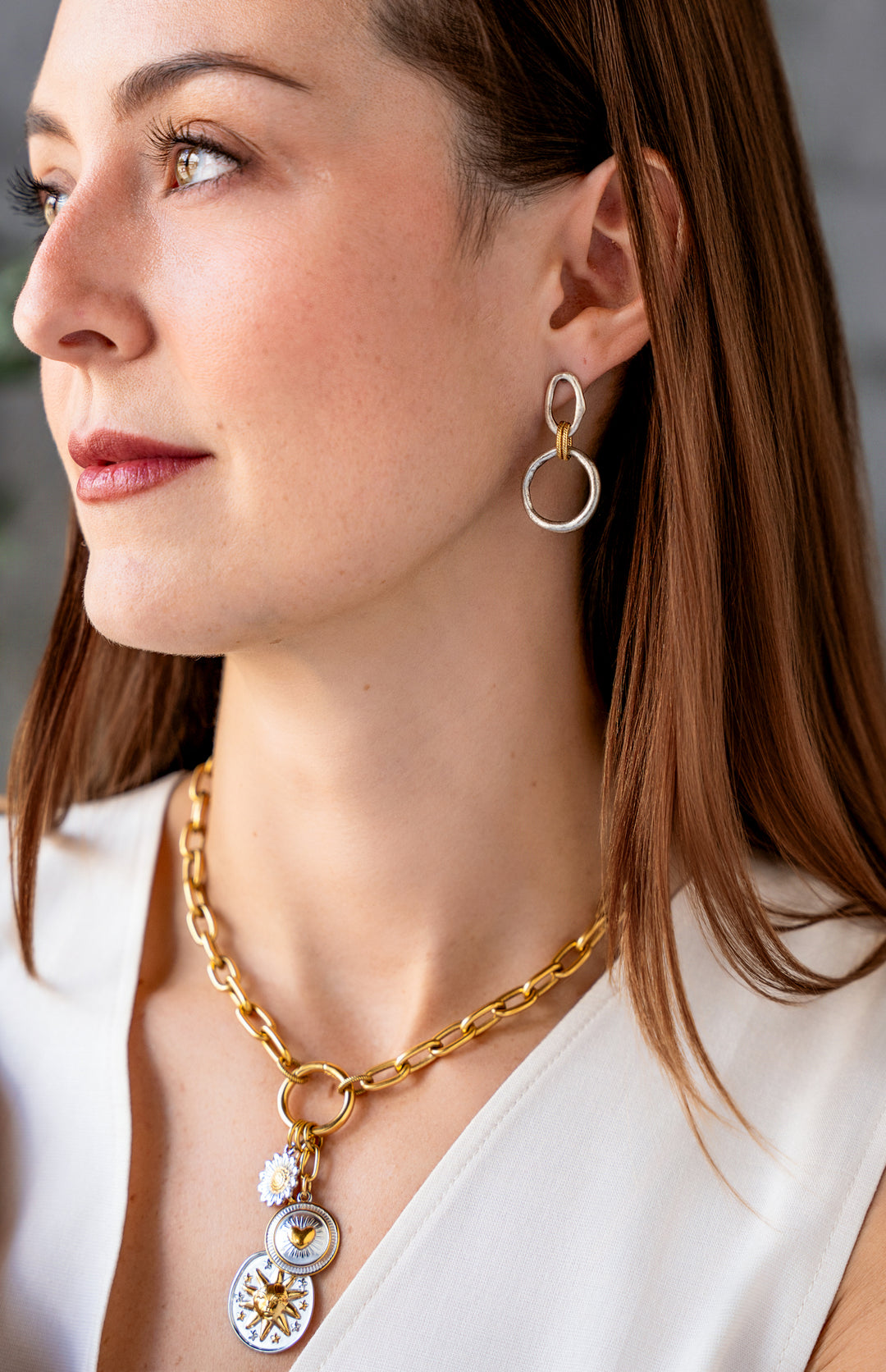 Mixed metal charm cluster necklace with sun medallion, heart charm, and daisy charm on a gold paperclip chain.