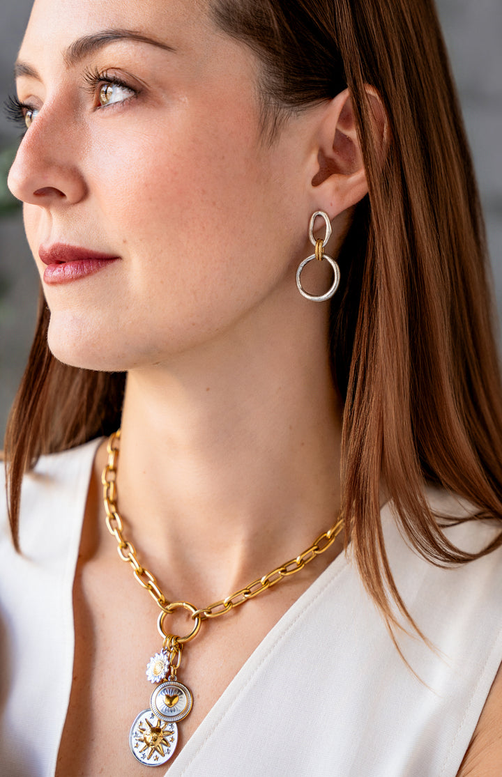 Mixed metal charm cluster necklace with sun medallion, heart charm, and daisy charm on a gold paperclip chain.