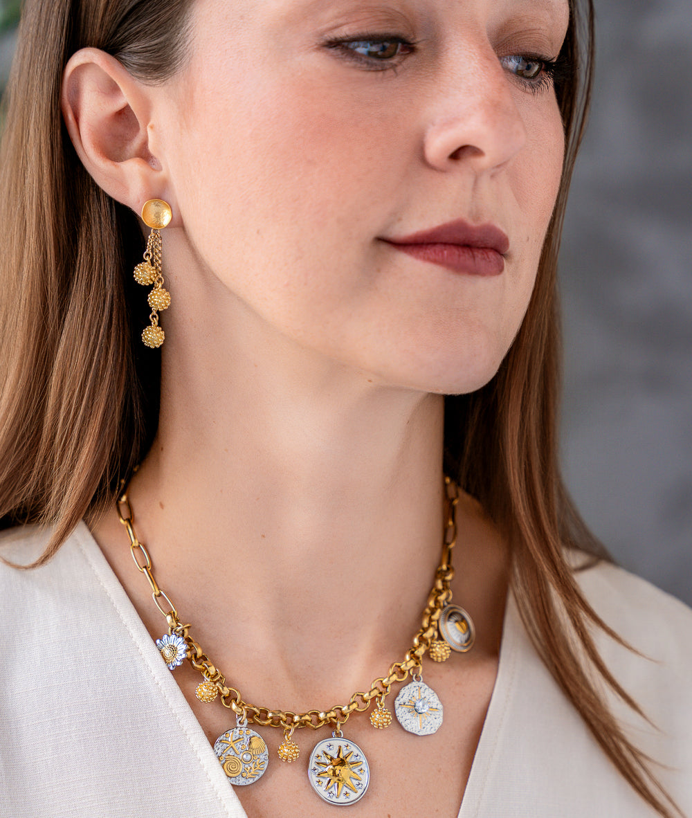 Mixed metal charm necklace with celestial, floral, heart, and ocean inspired charms hanging from a gold chain necklace.