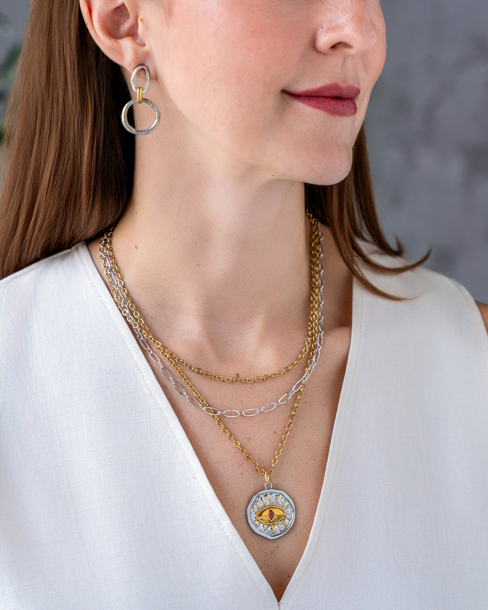 Mixed metal layered necklace with gold and silver chains and an eye pendant featuring a pink center stone.