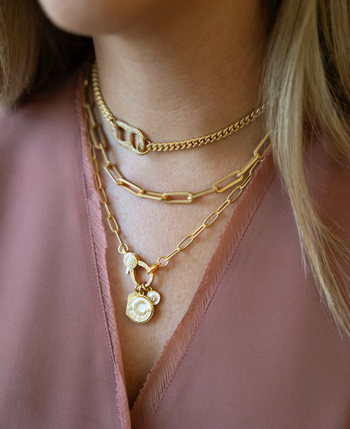 A matte gold paperclip chain necklace with a white moon, north star, and circle charm with a pave lobster claw.