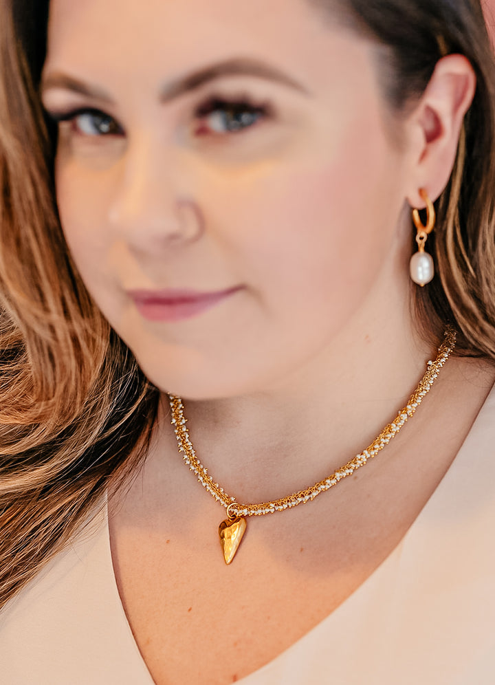 A model wearing A seed pearl drizzle necklace with a hammered heart pendant