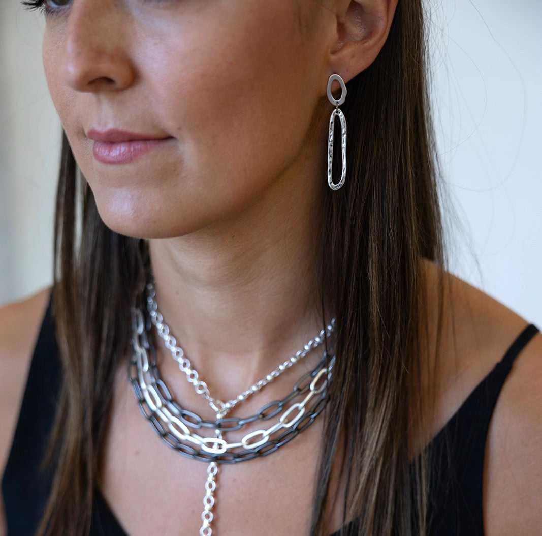 A model wearing A silver swirl dangle earring with oval cutout post.