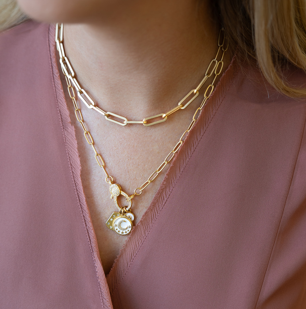 A matte gold paperclip chain necklace with a white moon, north star, and circle charm with a pave lobster claw.