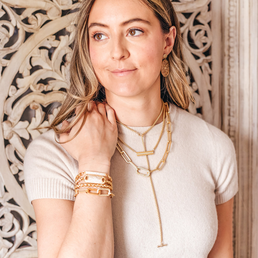 A woman modeling gold chainlink necklaces, bracelets, and earrings.