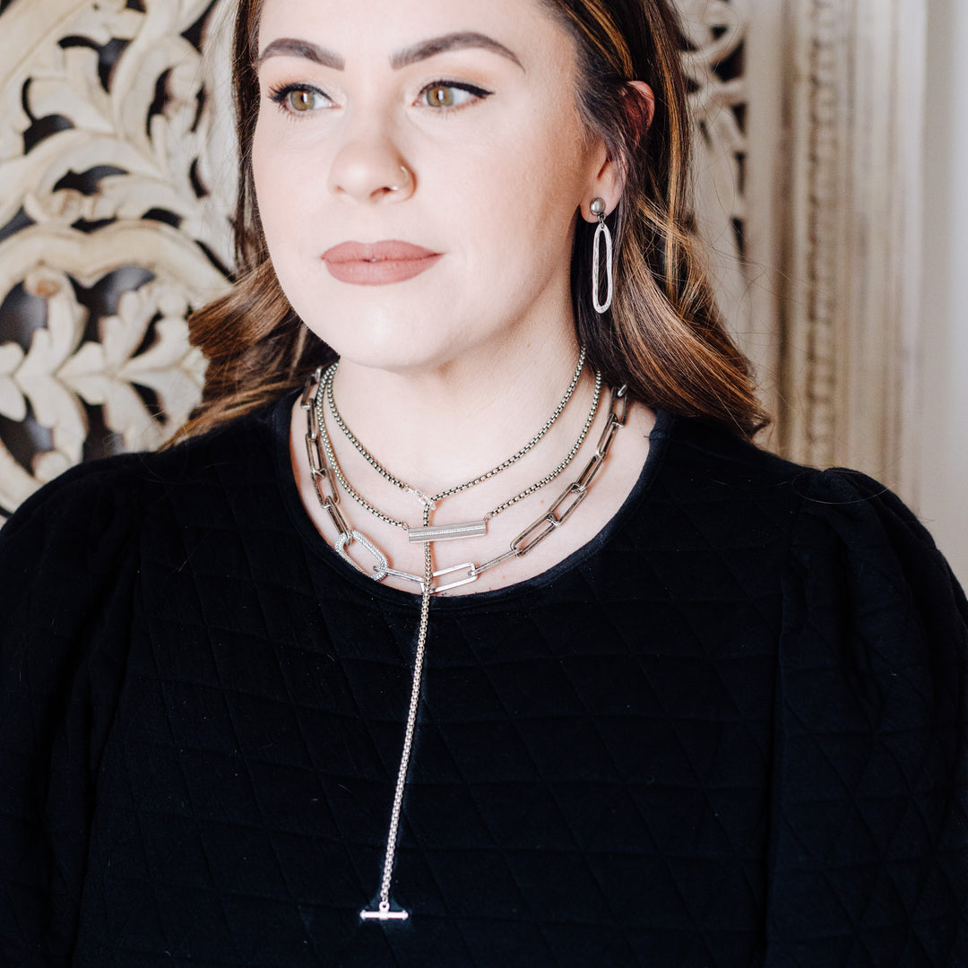 A woman modeling silver chainlink necklaces and earrings.