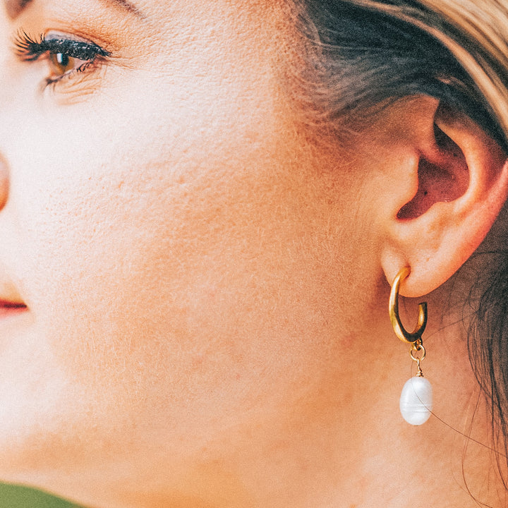 A model wearing a baroque pearl earring on gold ear loops.