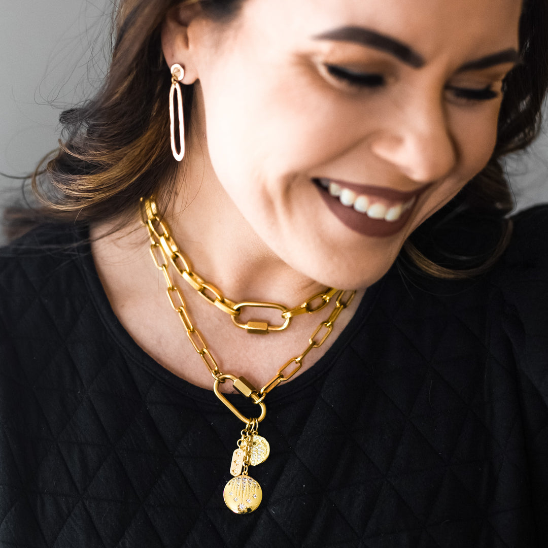 A model wearing gold layered chainlink necklaces with fireworks, hamsa, and star charms on a snap clasp.