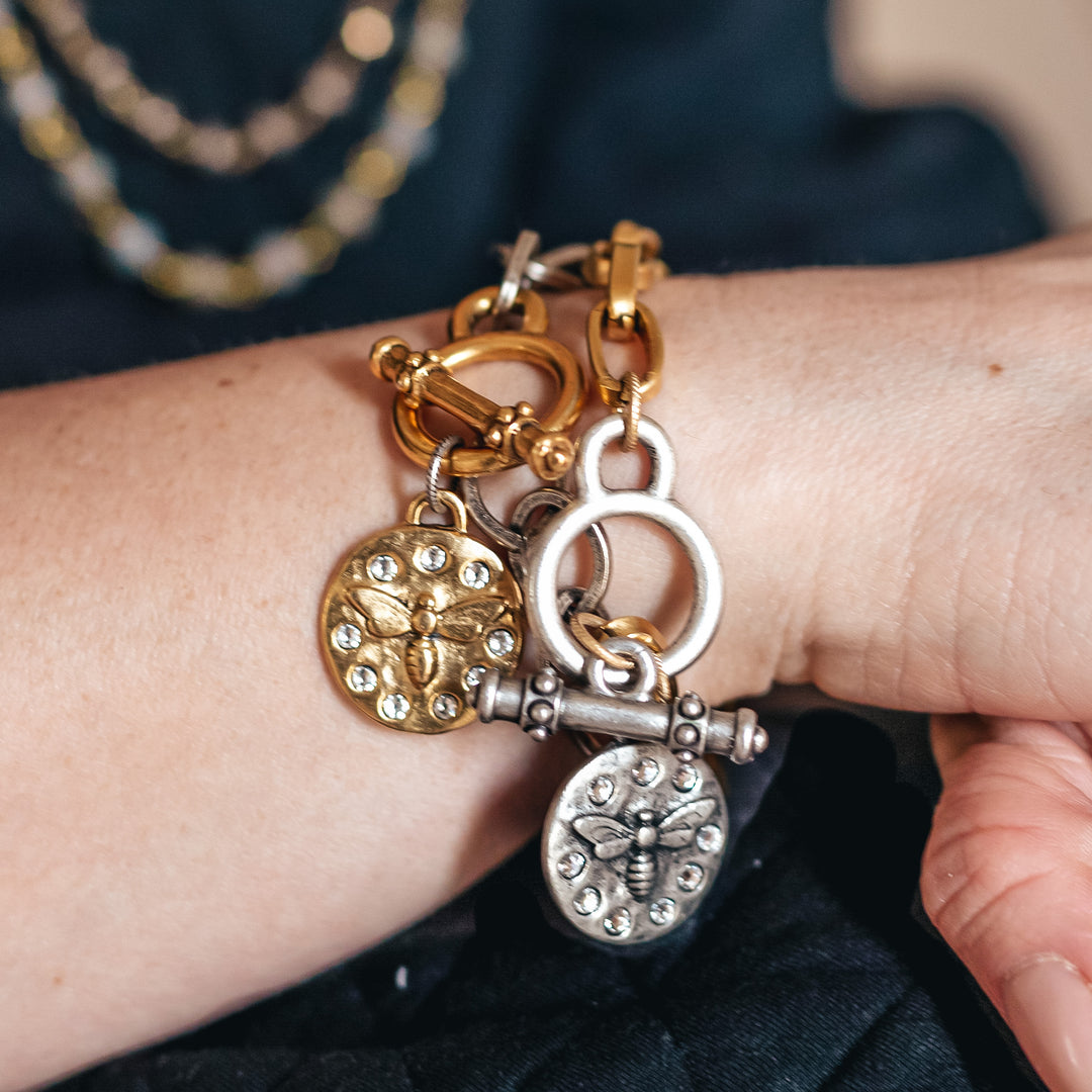 A woman's wrist modeling chainlink charm bracelets with bee pendant charms.