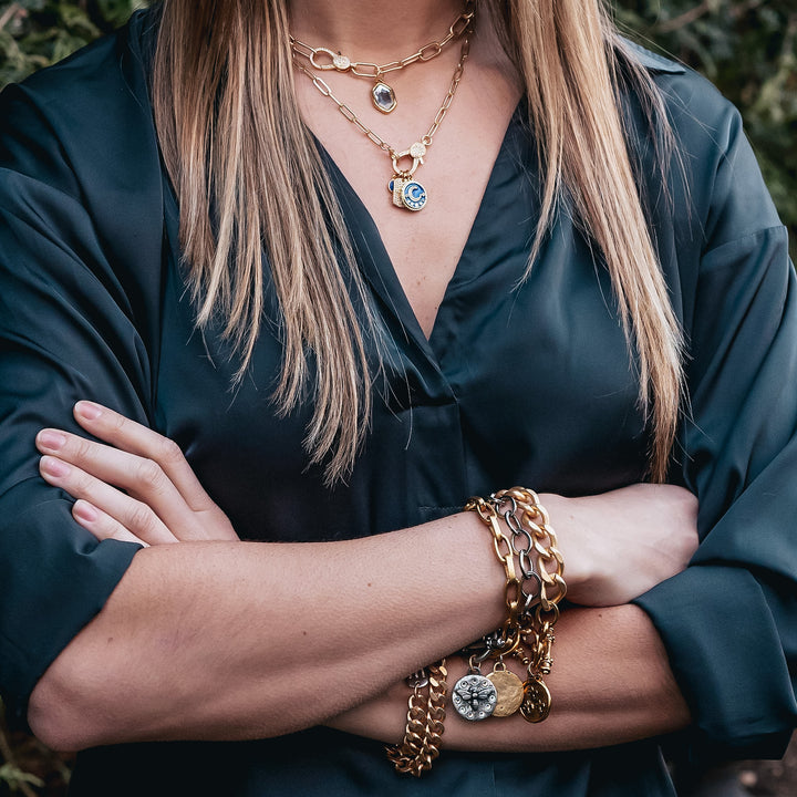 A model wearing layered paperclip chain necklaces with charm pendants and bracelets.