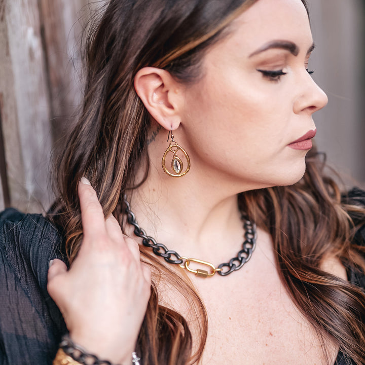 A model wearing a gunmetal chainlink necklace and gold dangle earrings.