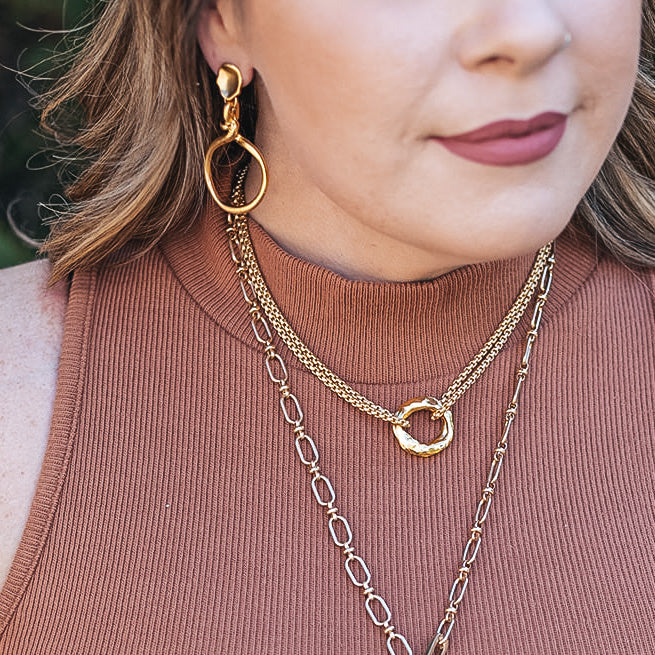 a matte gold dangle earring with a rope lasso detail