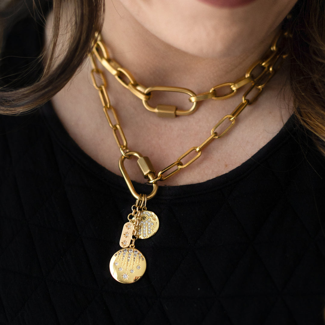 A model wearing gold layered chainlink necklaces with fireworks, hamsa, and star charms on a snap clasp.