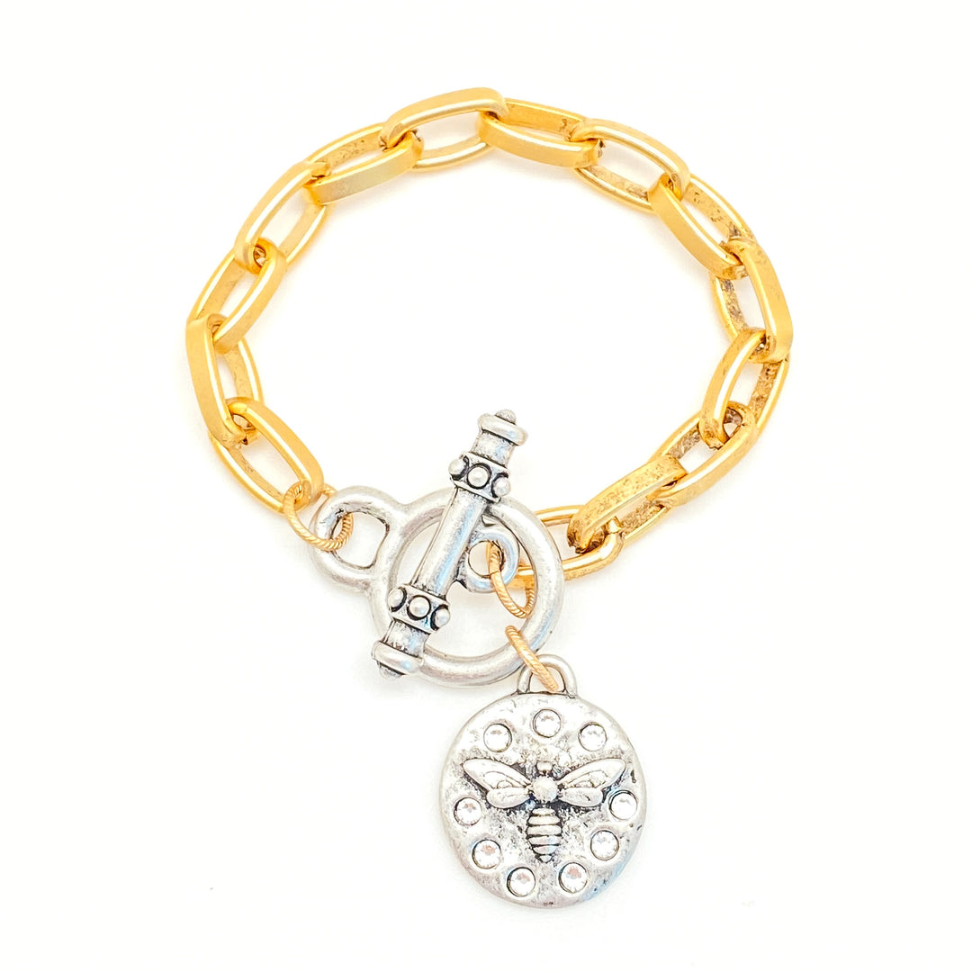 A gold paperclip link bracelet with a silver bee charm and toggle clasp.