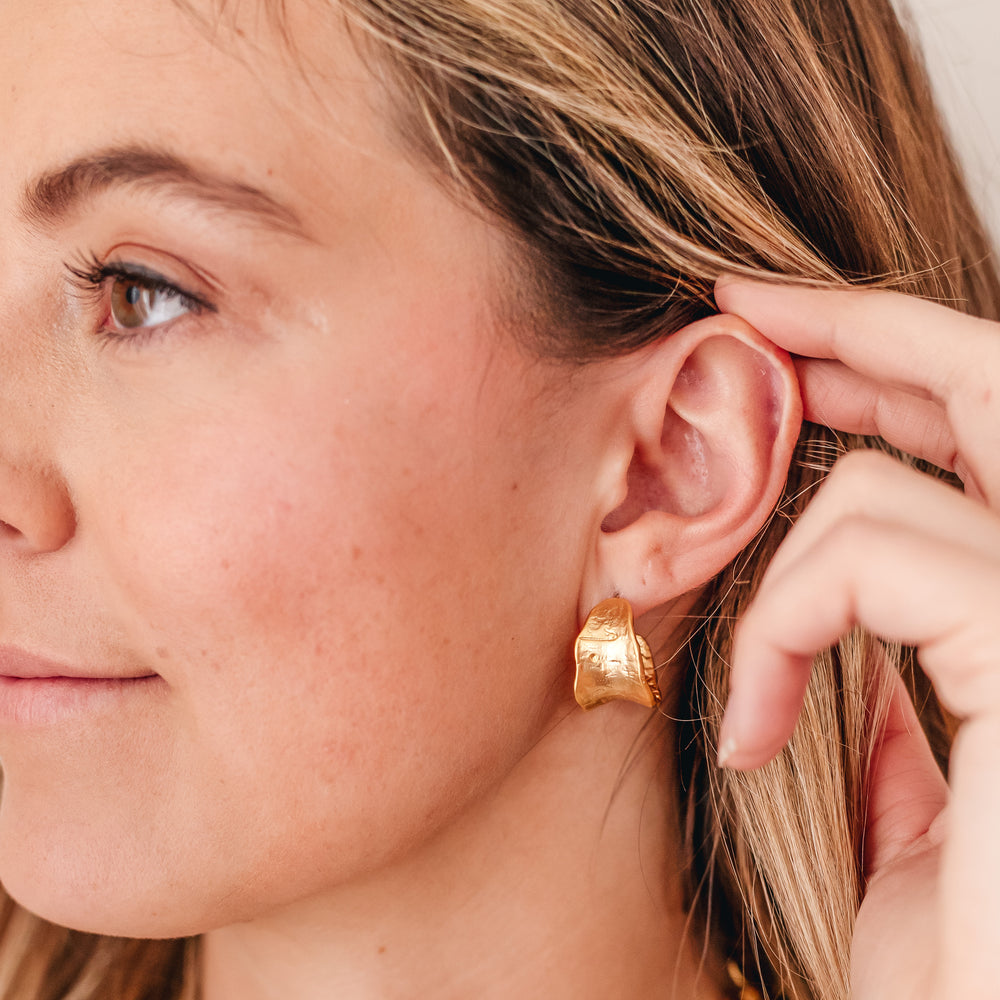 A model wearing matte gold post hoop earrings.