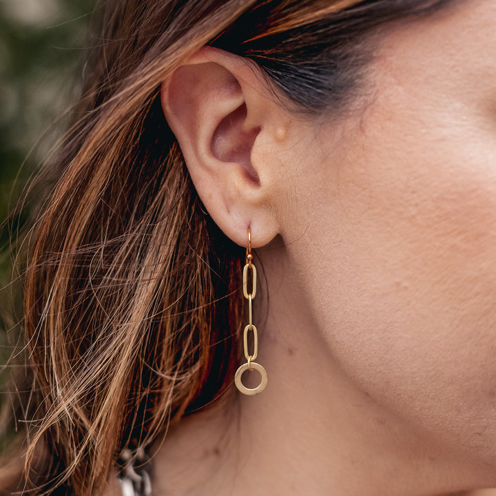 A model wearing a matte gold paperclip chain earrings with hoop detail.