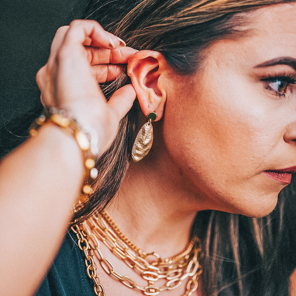 A model wearing layered chainlink necklaces, bracelets, and gold earrings.