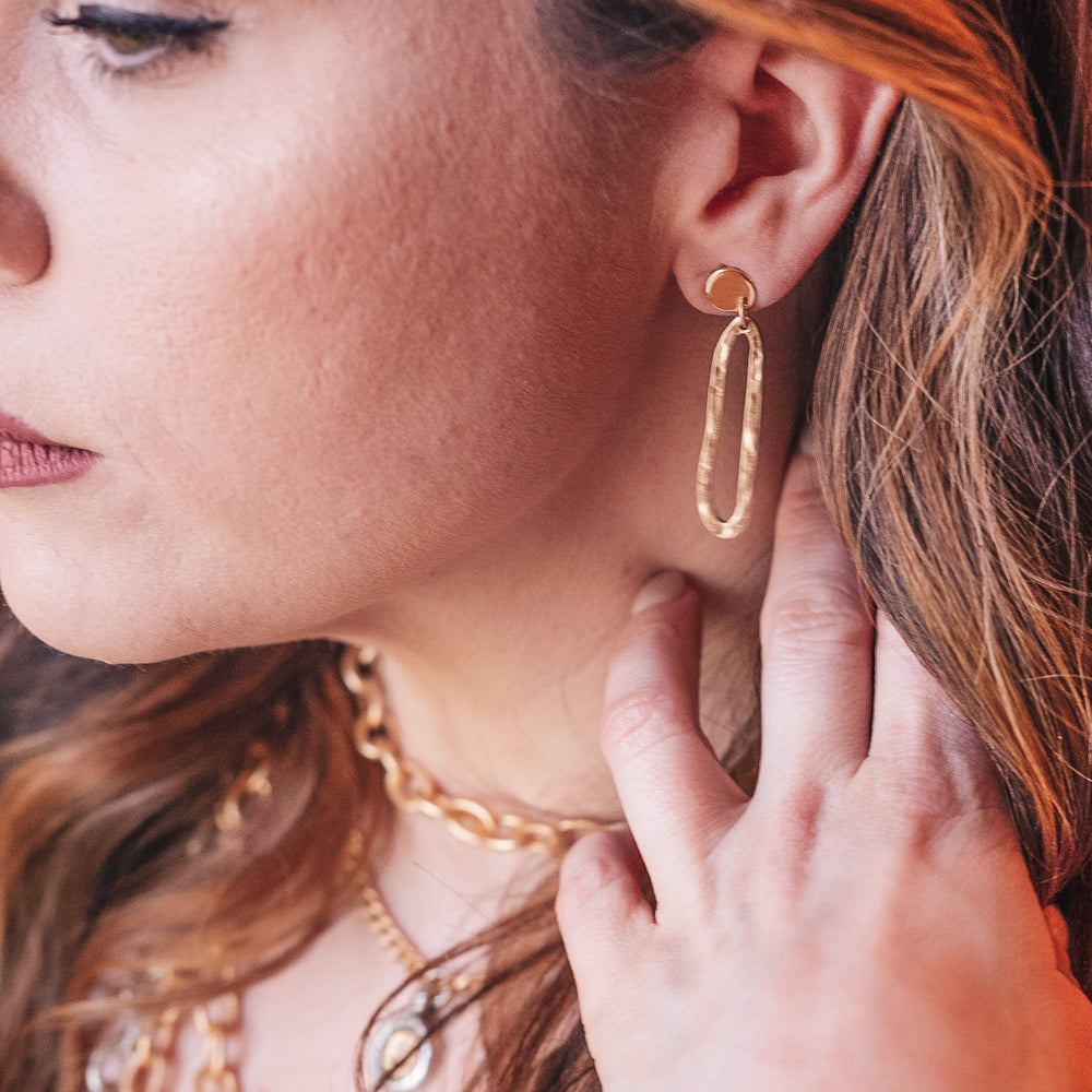 A model wearing a matte gold swirl drop earring.