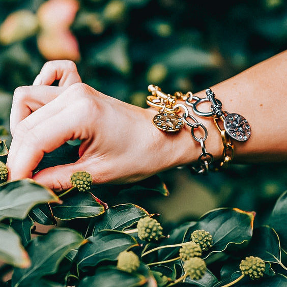 A woman's wrist modeling chainlink charm bracelets with plant background.