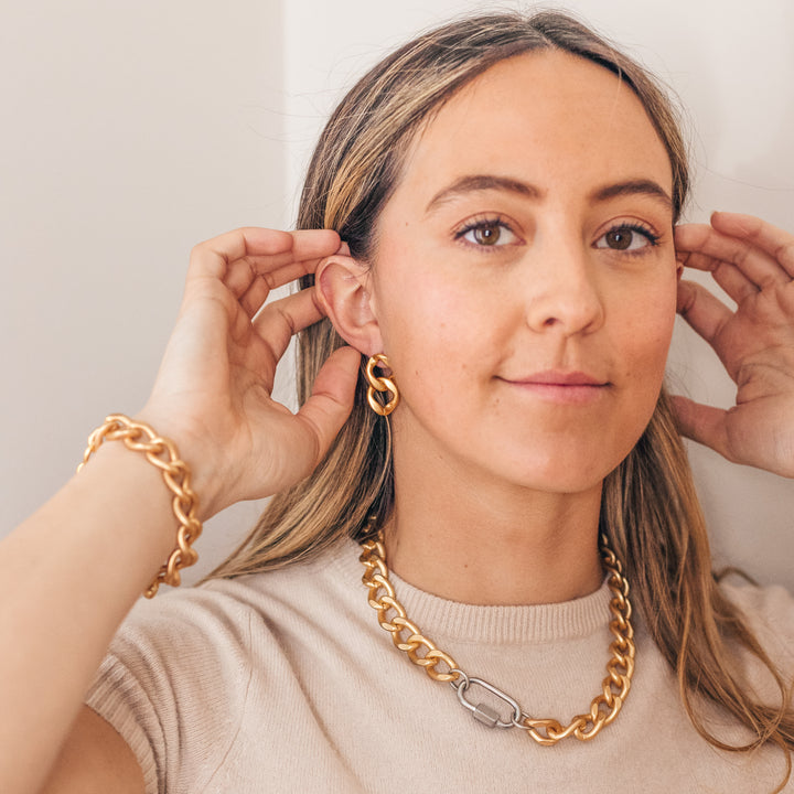 A girl wearing a large matte gold chain earrings, chainlink necklace, and chainlink bracelet.