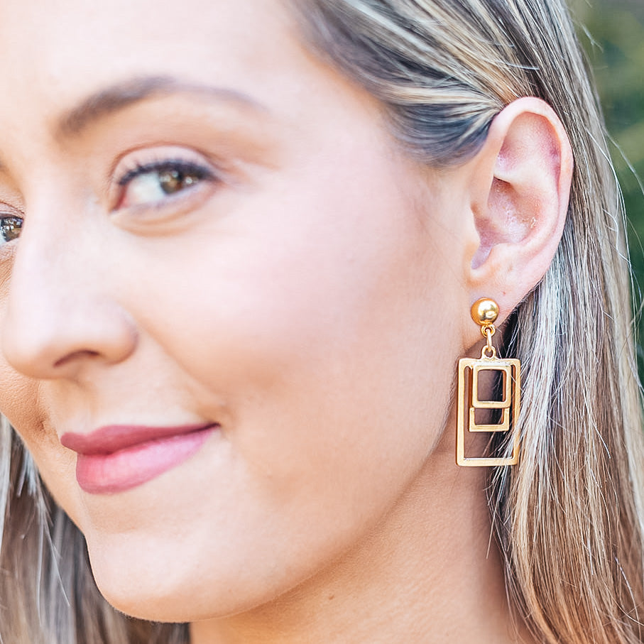 a model wearing A nested rectangle matte gold post earrings