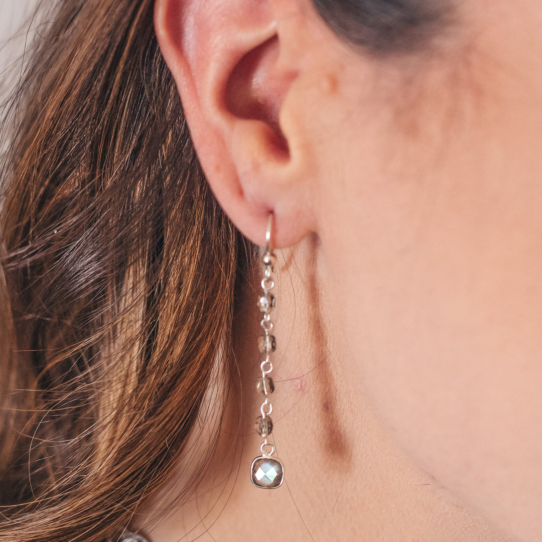 A model wearing a drop on gray crystal chain labradorite earring.