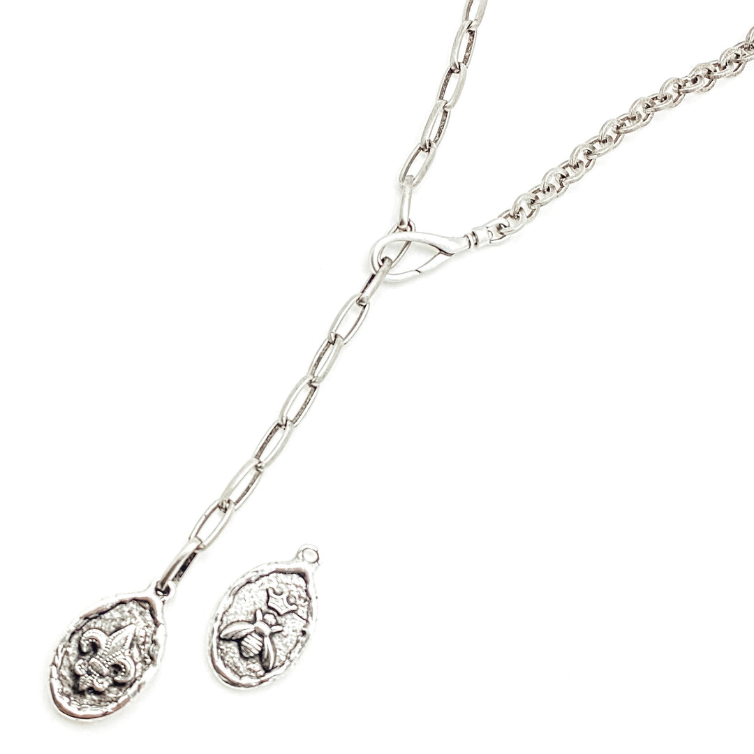 A silver mixed chain lariat necklace with a two sided bee and fleur de lis coin pendant.
