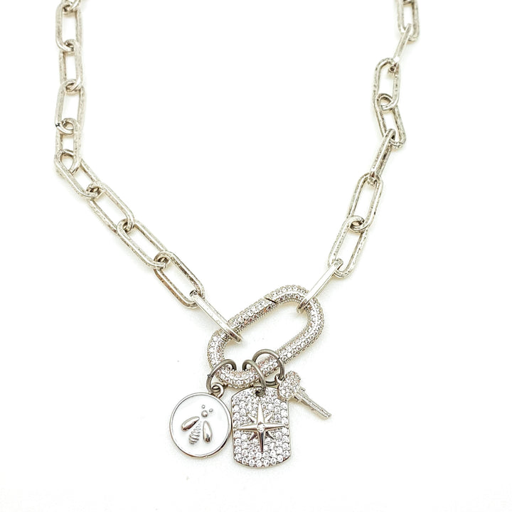 A silver paperclip necklace with pave carabiner and white bee, pave north star, and key charms.