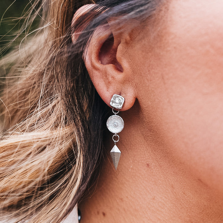 a silver dangle earring with a shield and round crystal connector